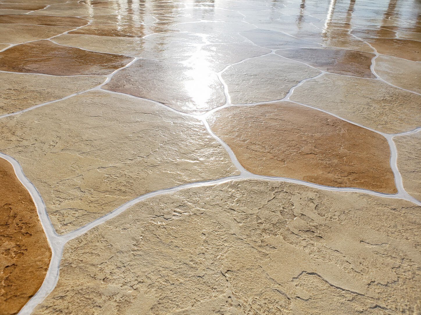 Tan colored stamped concrete driveway overlay with a sealed flagstone finish