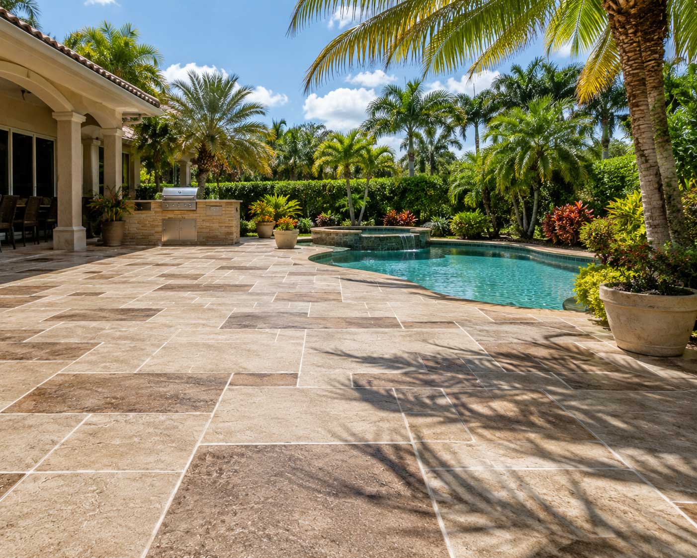 Tan stone paver pool deck with a raised spa and outdoor kitchen in Palm Beach and Broward County