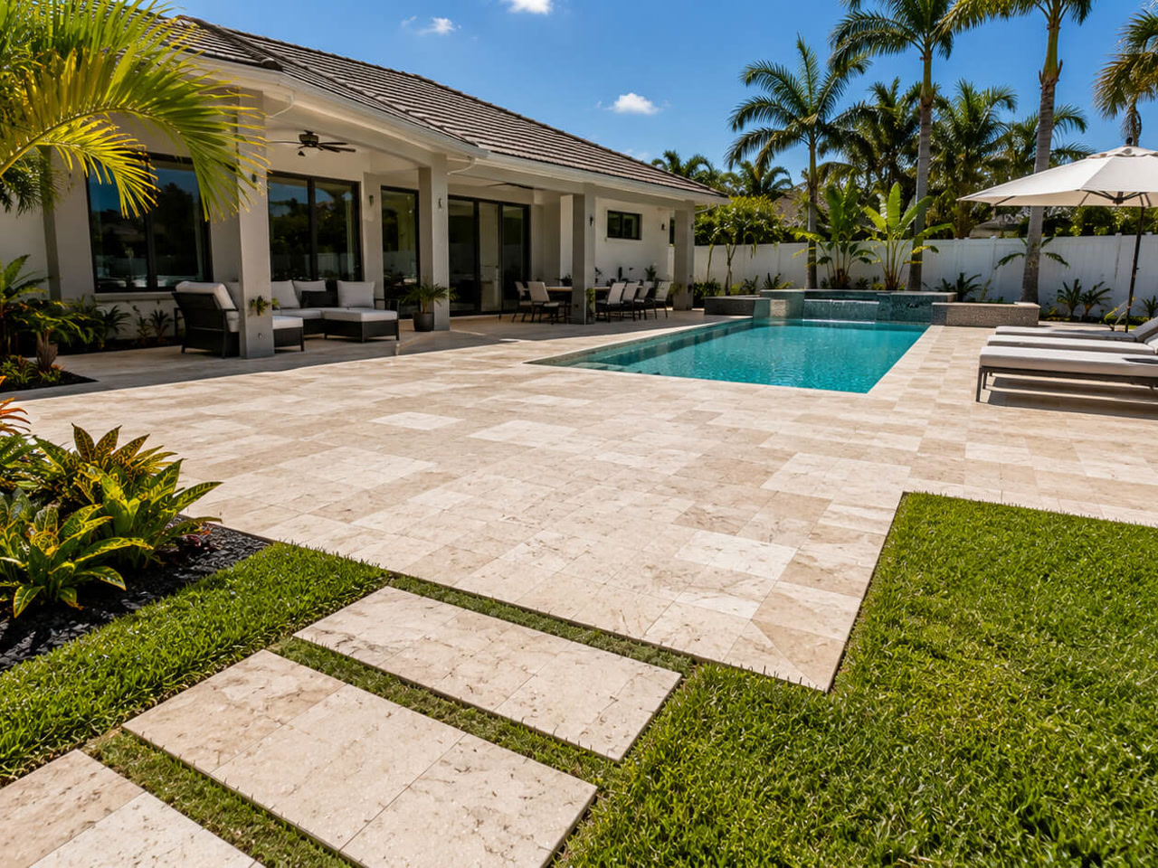 Travertine paver patio beside a pool with a stepping stone walkway leading to the lawn at a Loxahatchee property