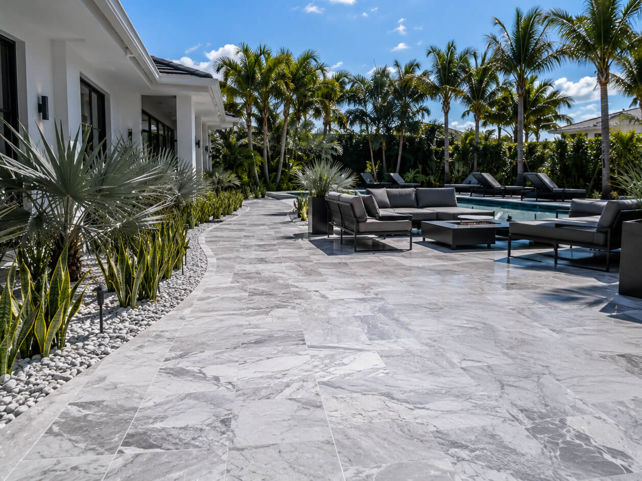 Gray marble paver patio curving along a modern home to a poolside lounge with a fire table in West Palm Beach