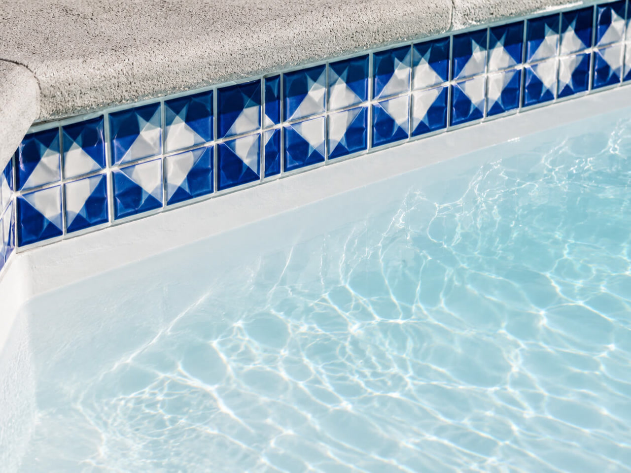 Classic white plaster pool finish under a blue and white patterned tile border and textured concrete coping in a Boca Raton pool