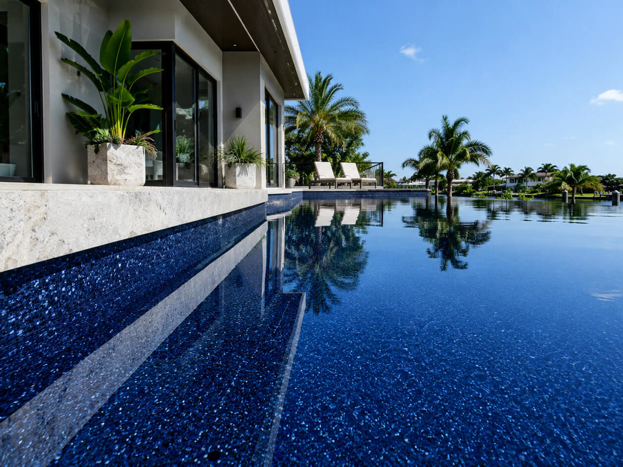 Finished pool resurfacing in a dark pebble finish, with sheer descents spilling in over gray marble coping at a Gulfstream home