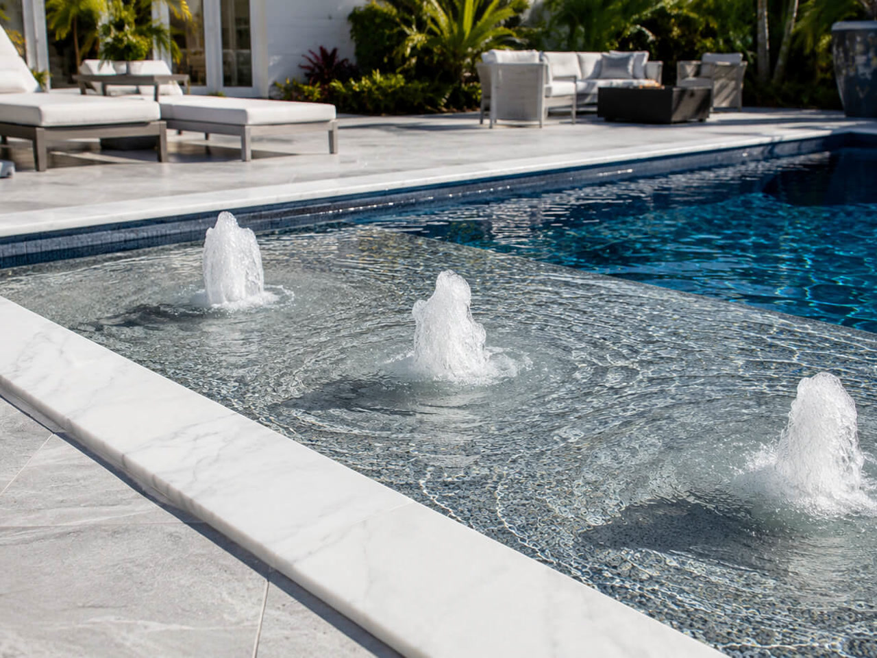 Bubblers lined up across a mosaic tiled sun shelf edged in white marble coping at a Gulfstream home
