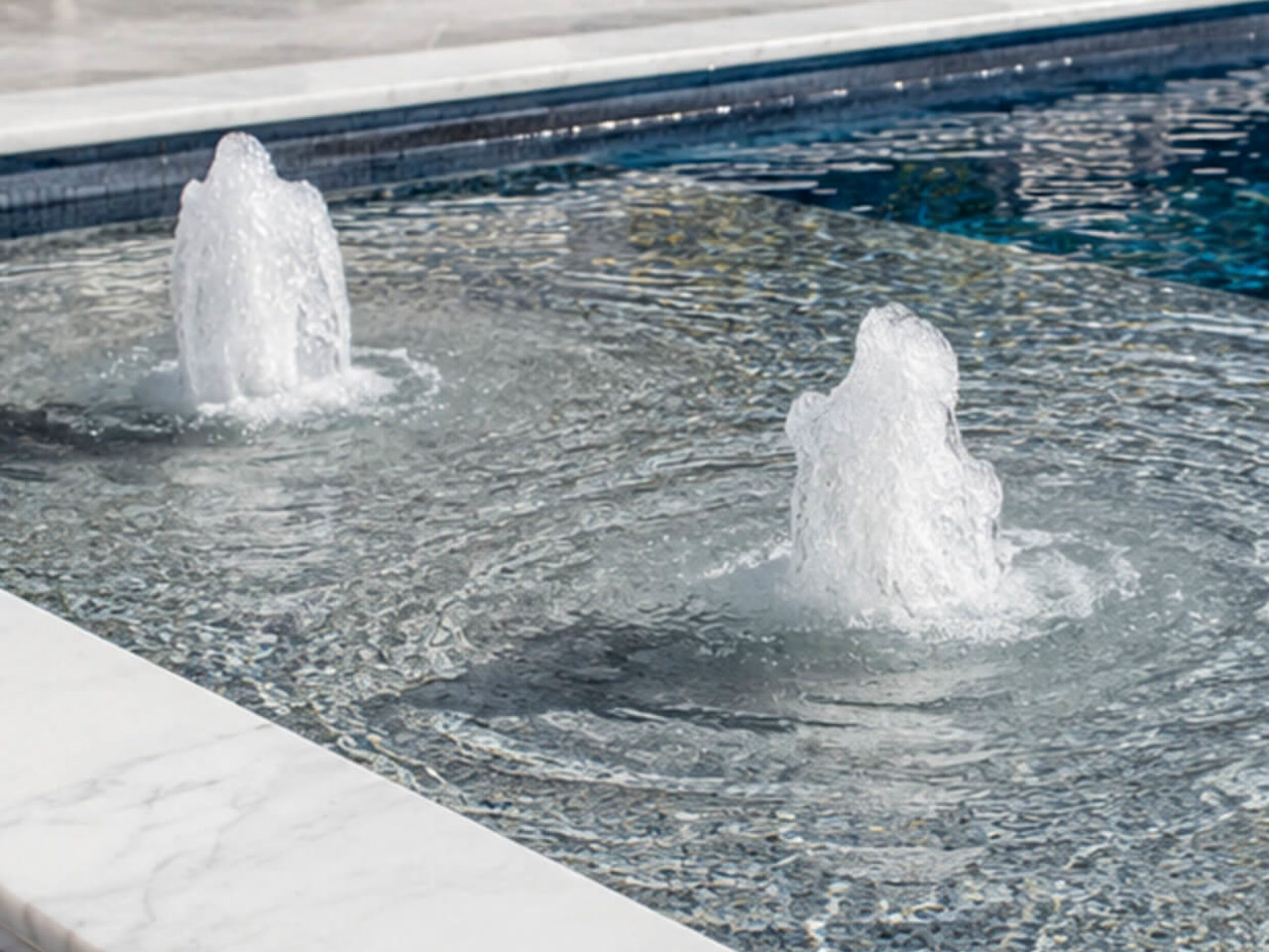 Two bubbler fountains on a mosaic tiled sun shelf edged with white marble coping for a Hypoluxo homeowner