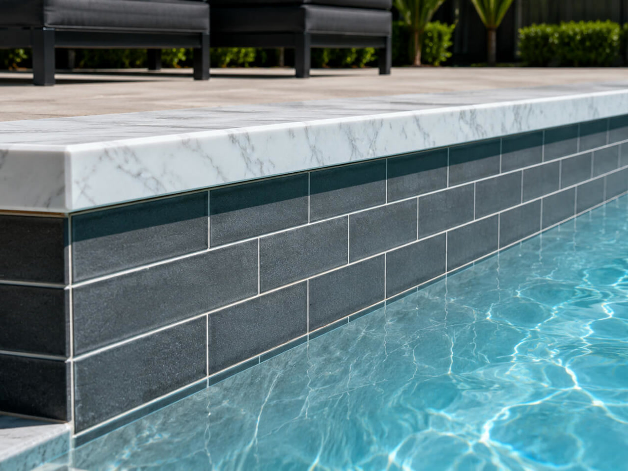White marble coping cap over charcoal subway tile along a pool wall in Deerfield Beach