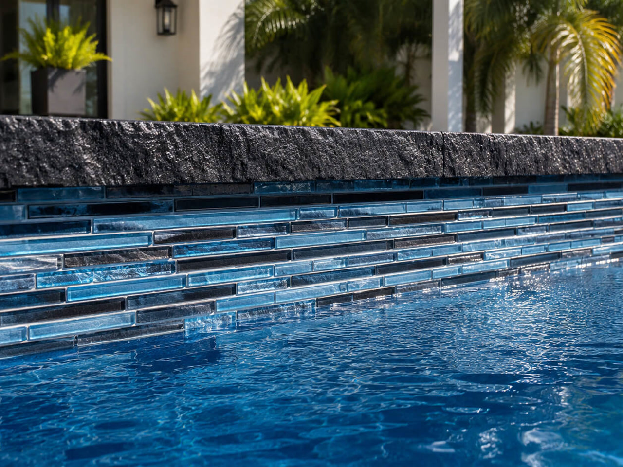 Finished pool edge with a rough cut black stone coping over linear blue glass waterline tile for a Greenacres homeowner