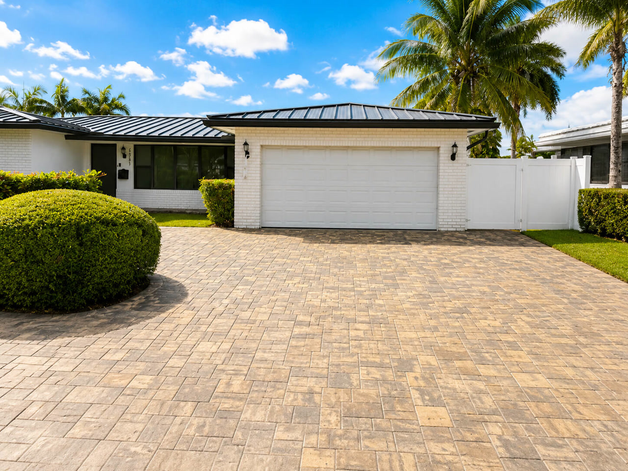 Paver driveway in a beige running bond pattern at a white brick Florida home with a black standing seam metal roof