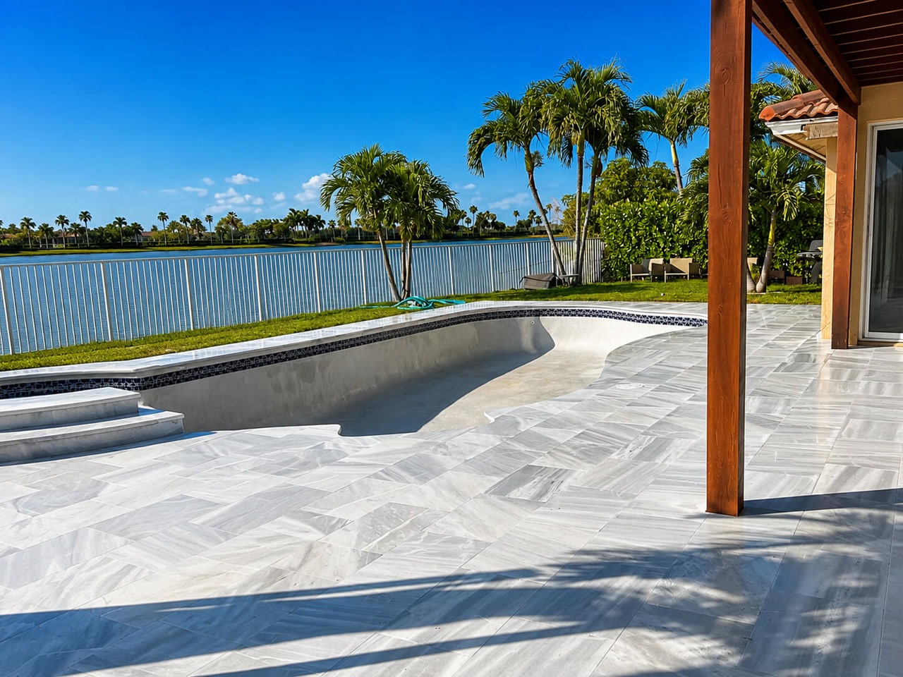Pool under construction with the new white marble paver deck already installed, overlooking a lake