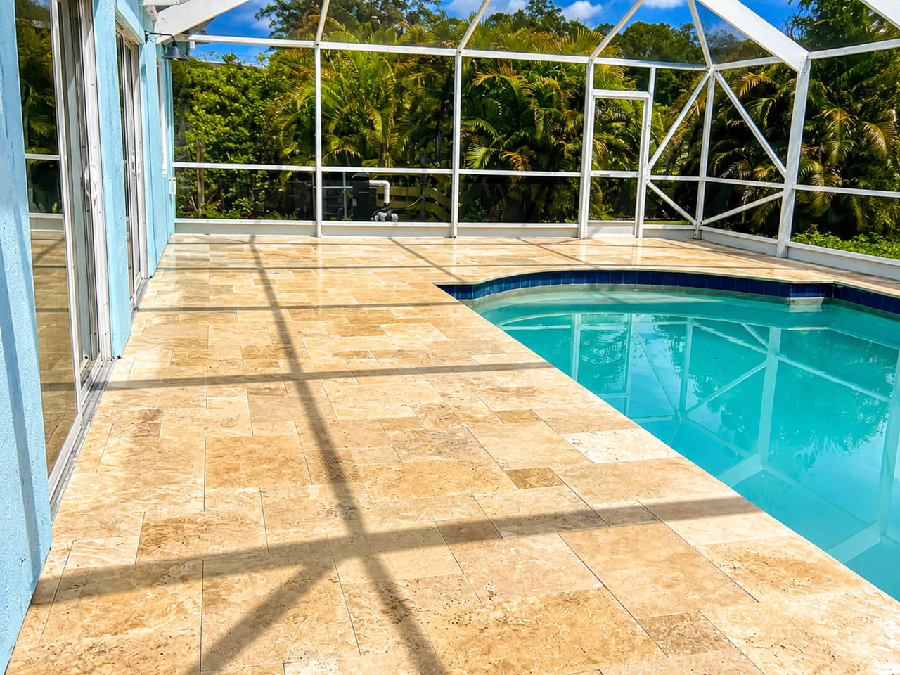 Sand toned travertine paver pool deck under a white screen enclosure, with dark blue tile coping along the pool