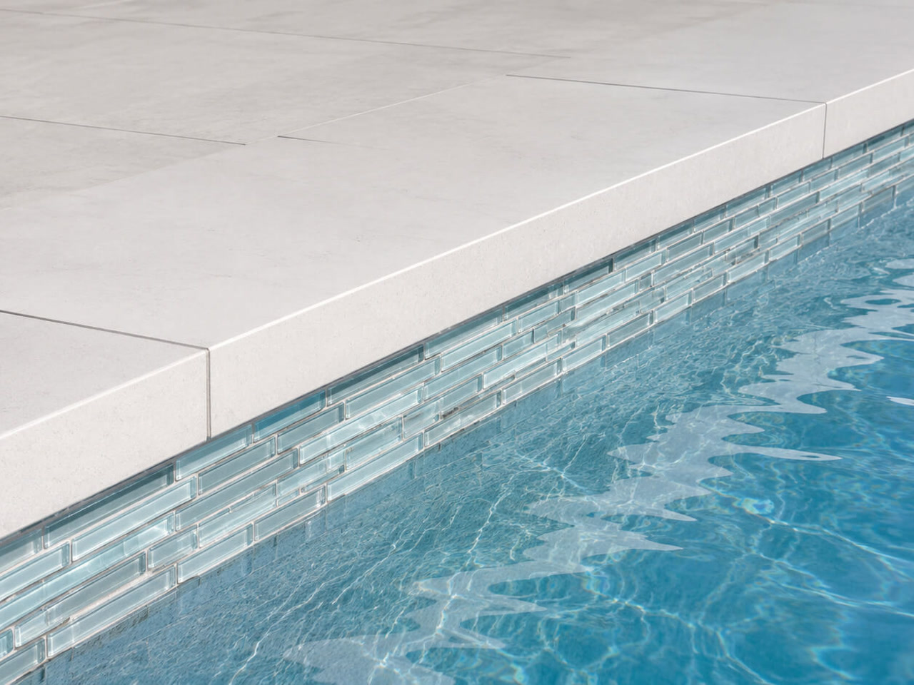 Squared off light stone coping over a band of linear pale blue glass waterline tile